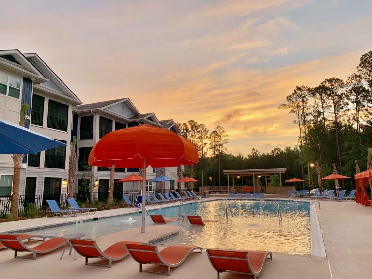 A pool with lounge chairs and umbrellas at sunset available at the 42 Apartment Property Management.