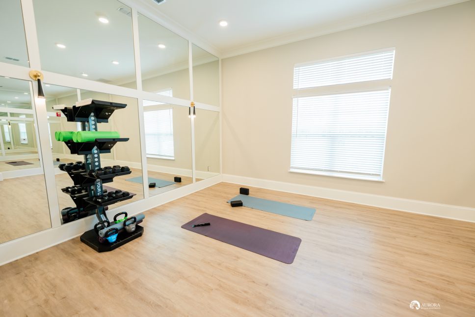 A gym room with mirrors and a yoga mat is available at the 42 Apartment Property Management.
