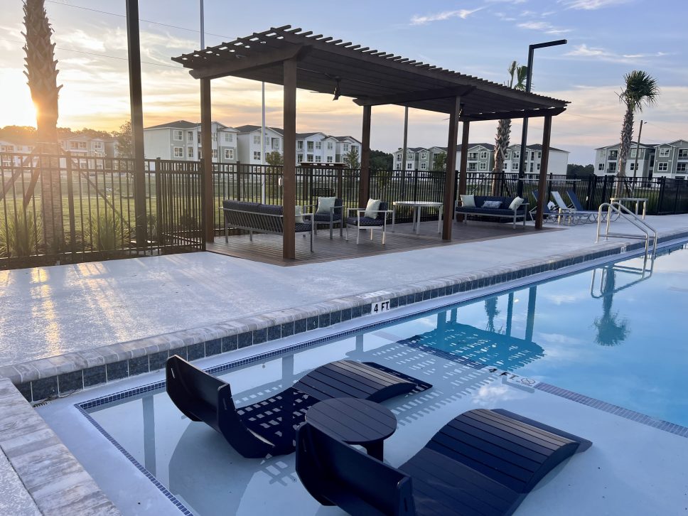 A pool with lounge chairs and a gazebo at sunset on a 42 Apartment Property Management.