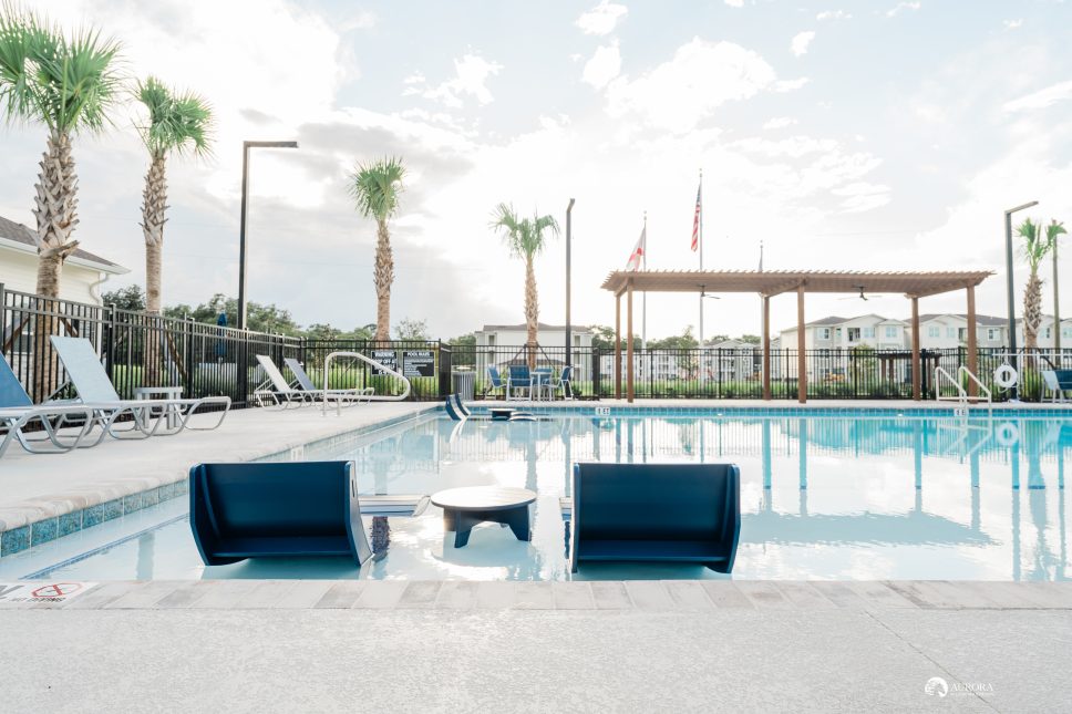 A swimming pool with lounge chairs and palm trees, located within the 42 Apartment Property Management complex.