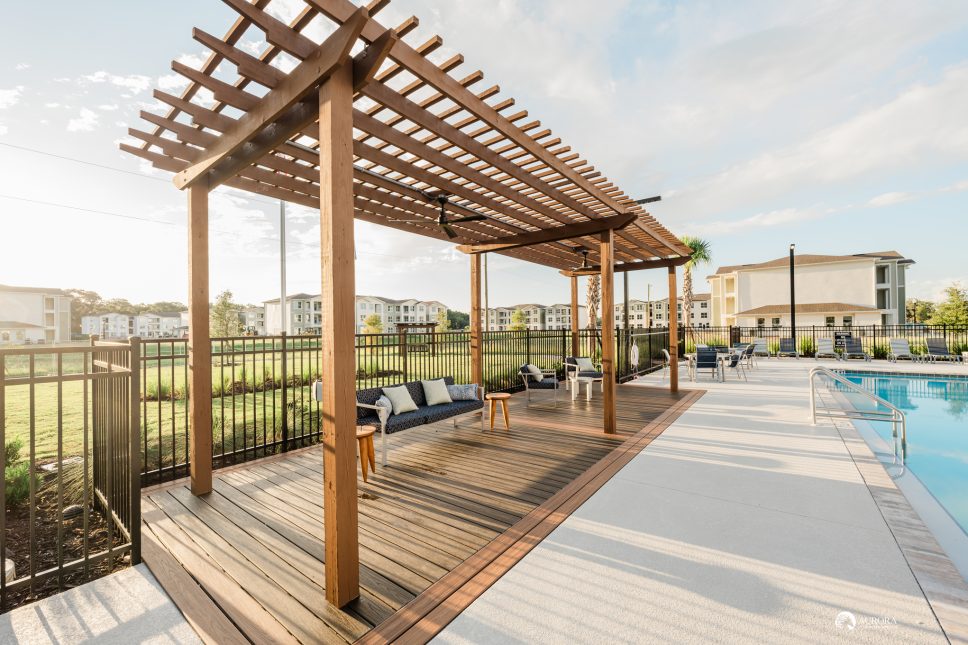 A wooden deck with a pergola overlooking a swimming pool, perfect for residents of the 42 Apartment Property Management to enjoy.