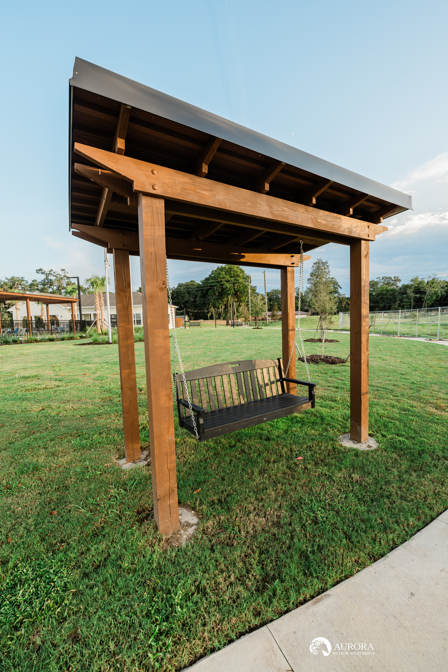 A wooden gazebo with a swing in the middle of a grassy area, managed by 42 Apartment Property Management.
